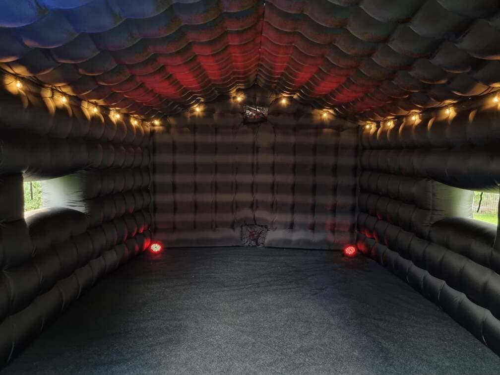 Interior of a large black inflatable room with string lights hanging inside and two rectangular windows on opposite walls.
