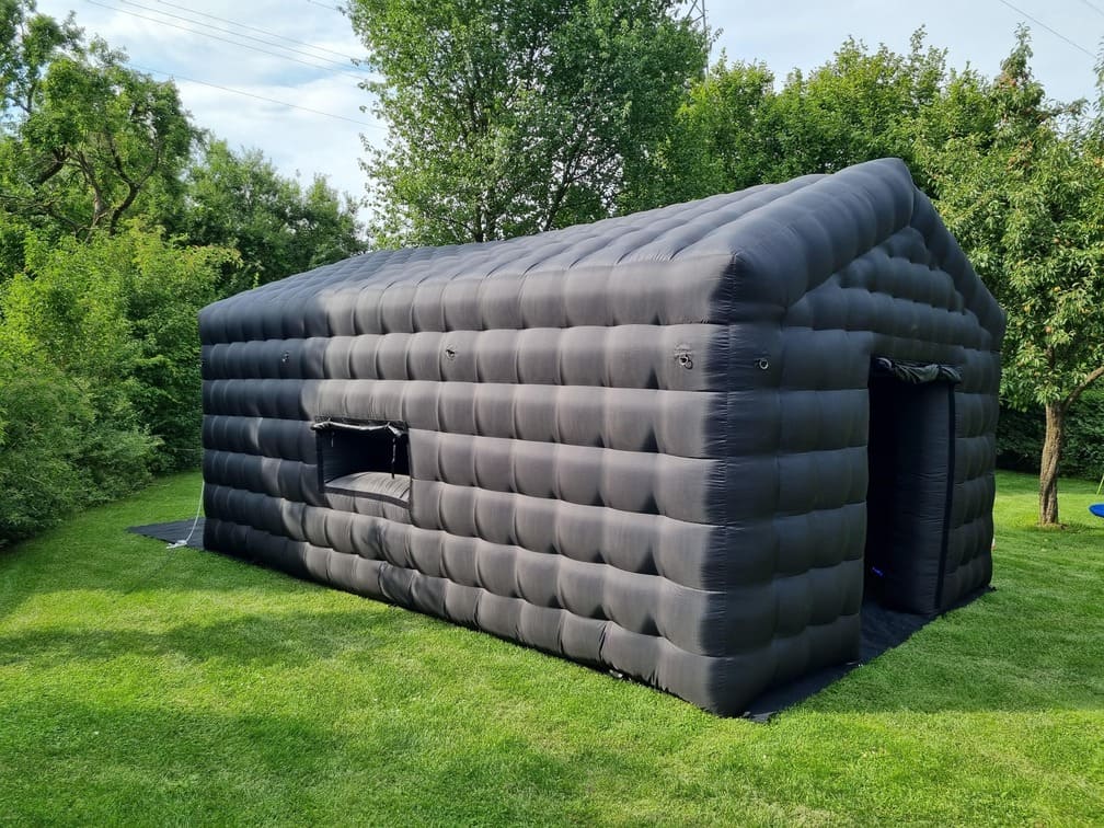 Large black inflatable tent set up on green grass surrounded by trees.
