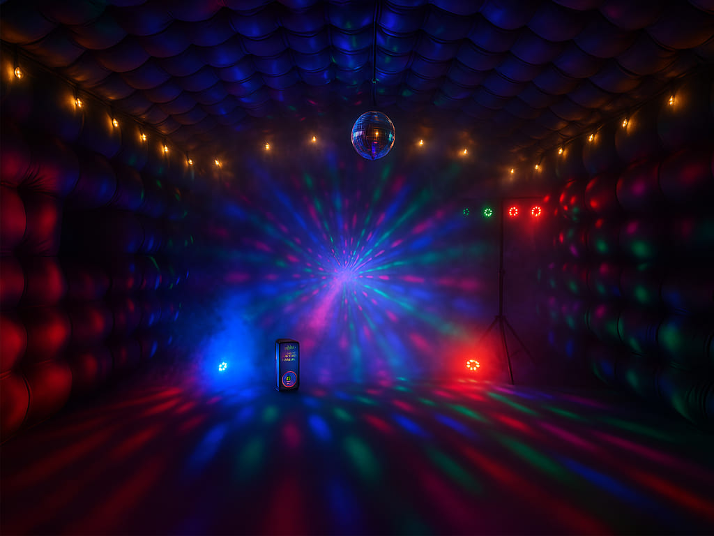Indoor dark room with colorful disco light patterns, a hanging disco ball, and small light fixtures emitting red, blue, and green lights.