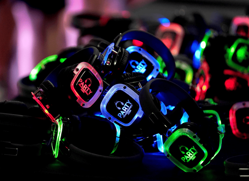 Multiple pairs of illuminated wireless headphones with colorful LED lights in red, blue, and green for a silent disco party.